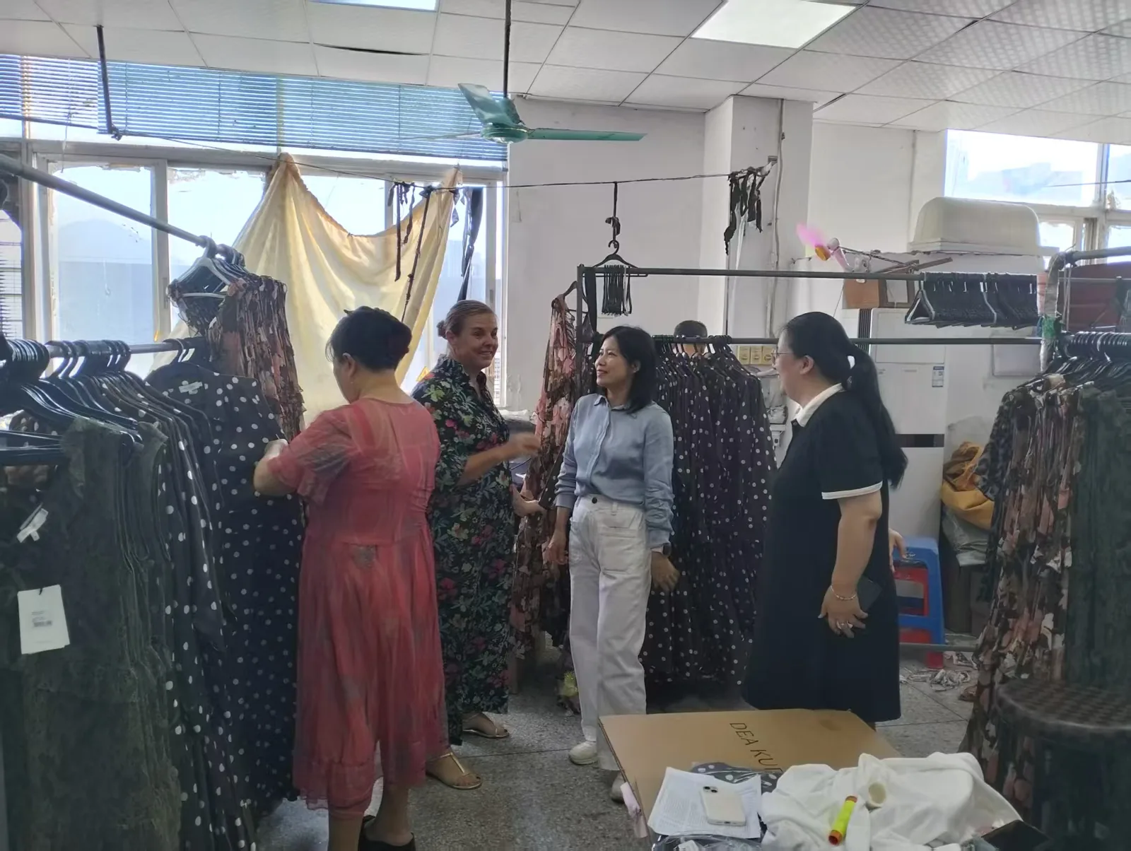 Un client européen et l’équipe NICOO examinant des vêtements en soie sur les portants lors d’une visite de l’atelier de Shenzhen